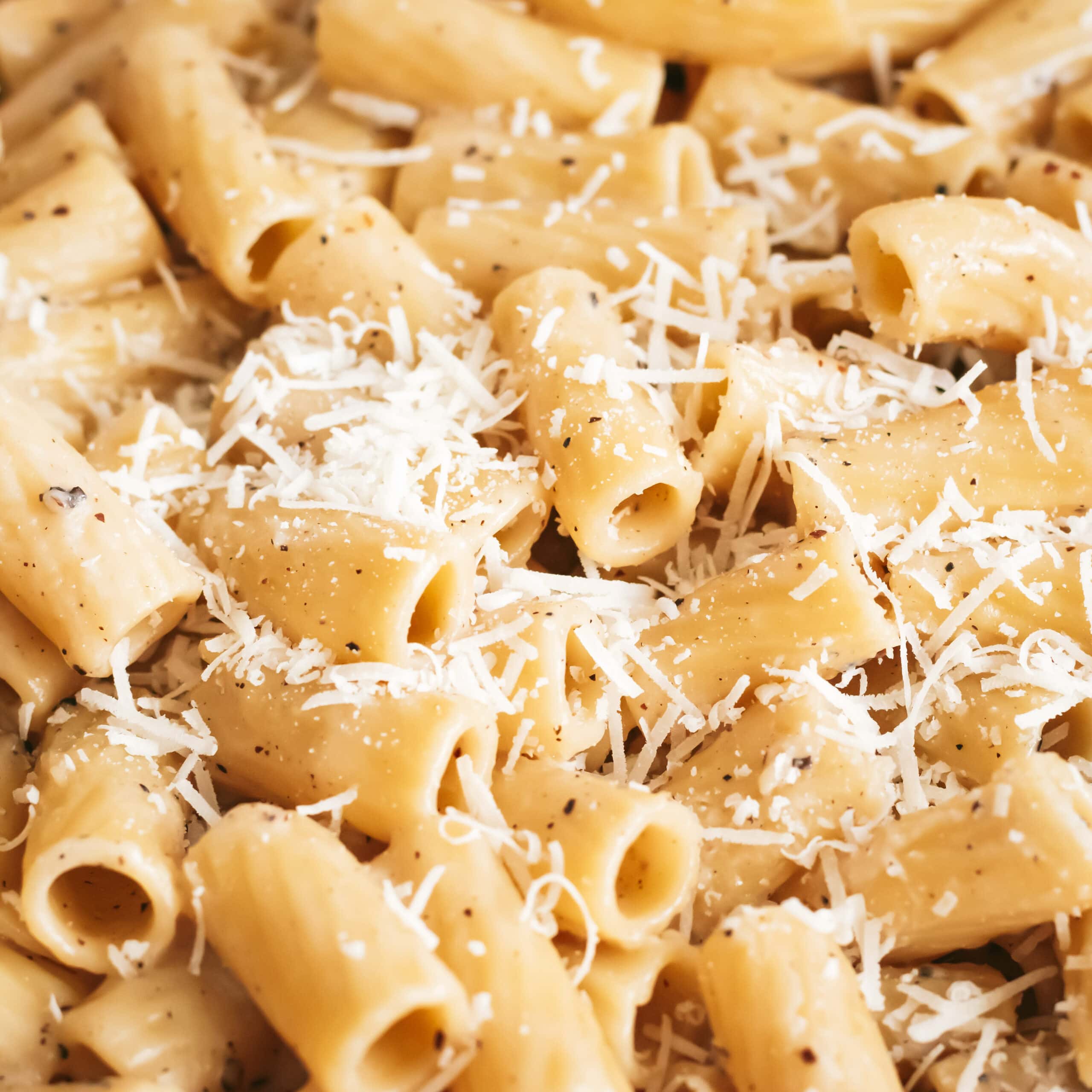 a close up of cheesy cacio e pepe rigatoni topped with grated pecorino and parmesan cheese